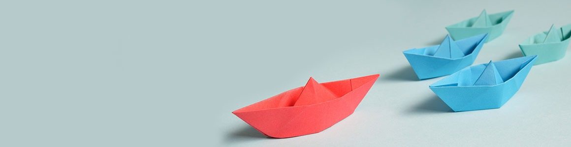 Red paper boat leading three blue paper boats