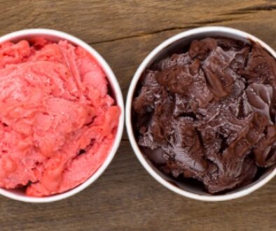 A variety of colorful ice creamed lined up in bowls with a wooden background.