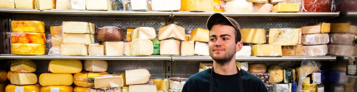 A man standing in front of specialty cheeses in a retail shop.