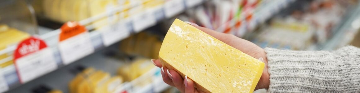 Woman picking out a brick of cheddar cheese at a grocery store.
