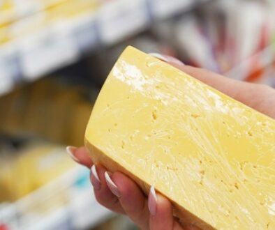 Woman picking out a brick of cheddar cheese at a grocery store.