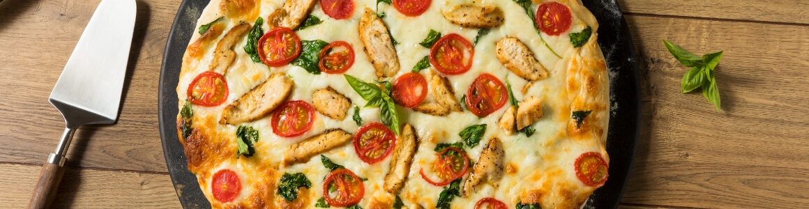White pizza topped with alfredo sauce, chicken, cherry tomatoes, and basil.