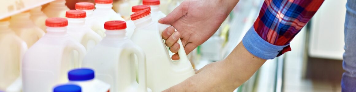 A person selecting a jug of milk from a grocery store.
