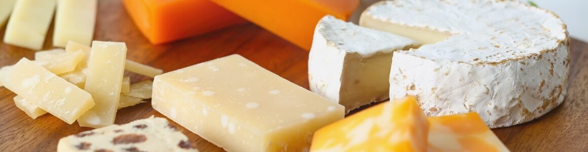 Assorted cheeses including brie, colby jack, parmesan, and cheddar on a wodden cutting board