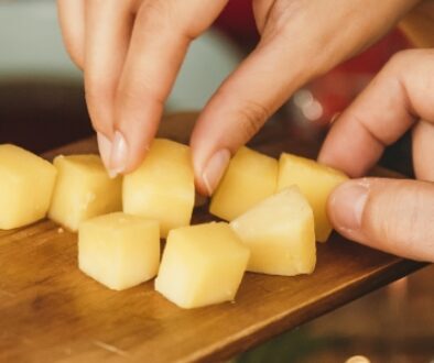 Hands reaching for bite-sized cheese cubes on a wooden serving board.